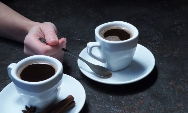 prikaz dve šoljice kafe i osobe koja drži malu kašičicu u ruci