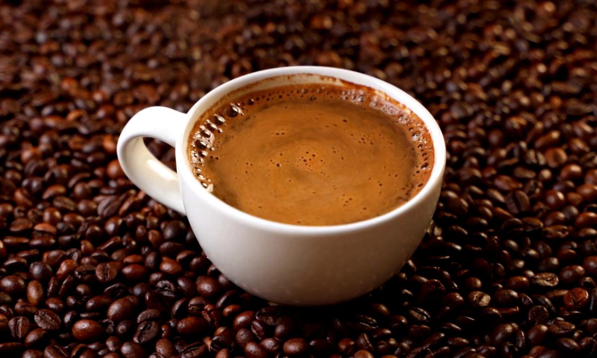šoljica crne kafe i zrna kafe okolo